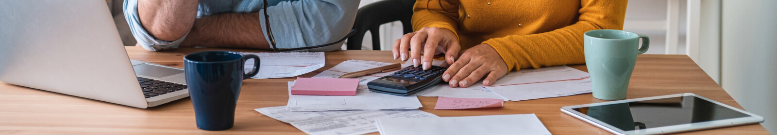 Close up of two people's hands using a calculator and a laptop